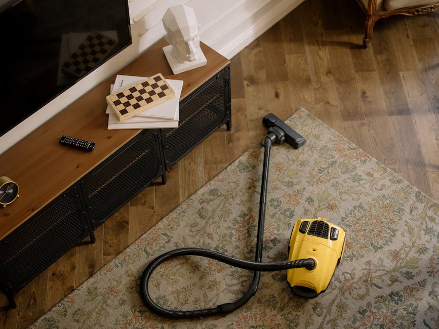 Two professional cleaners from Highbury Carpet Cleaners are preparing their equipment outdoors on paved ground, with one woman adjusting or examining a carpet cleaning machine with a white tank and ho