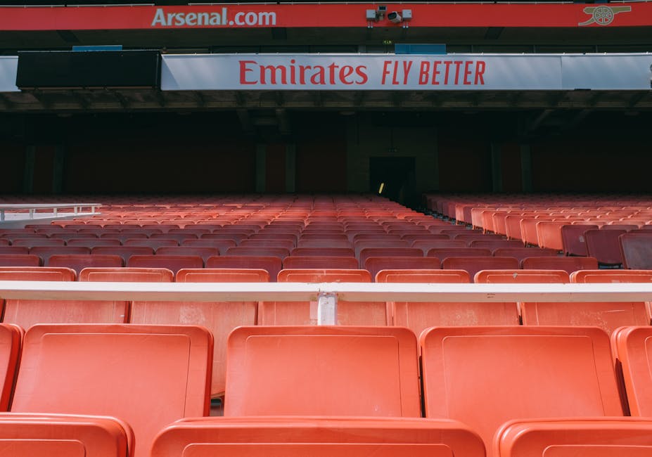 Interior view of Emirates Stadium taken from the upper tier, showcasing a well-maintained football pitch with vibrant green grass and precisely marked white lines for gameplay. The pitch appears fresh